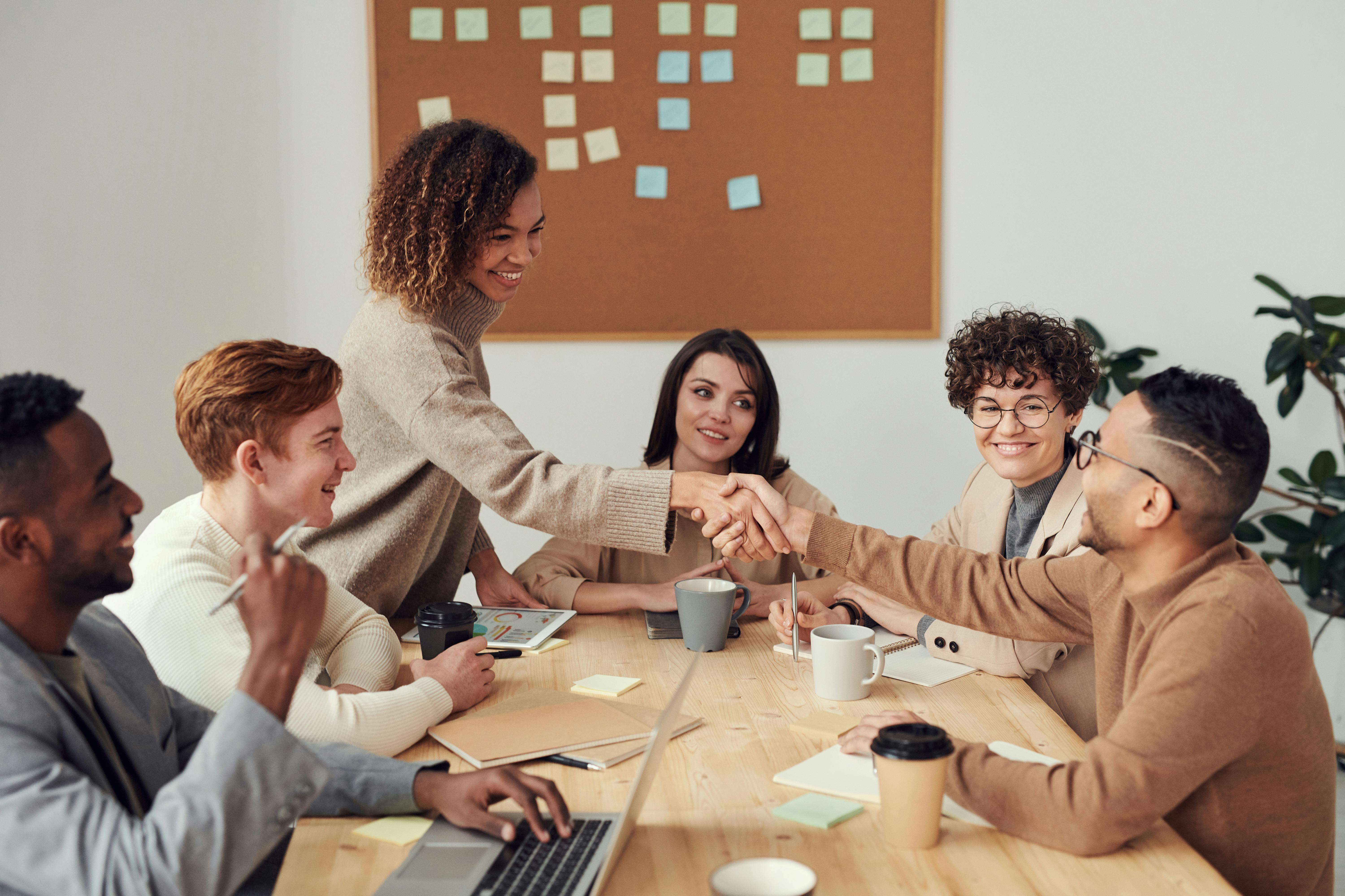 A team of professionals having a serious discussion in a modern office meeting room, looking at a laptop screen.